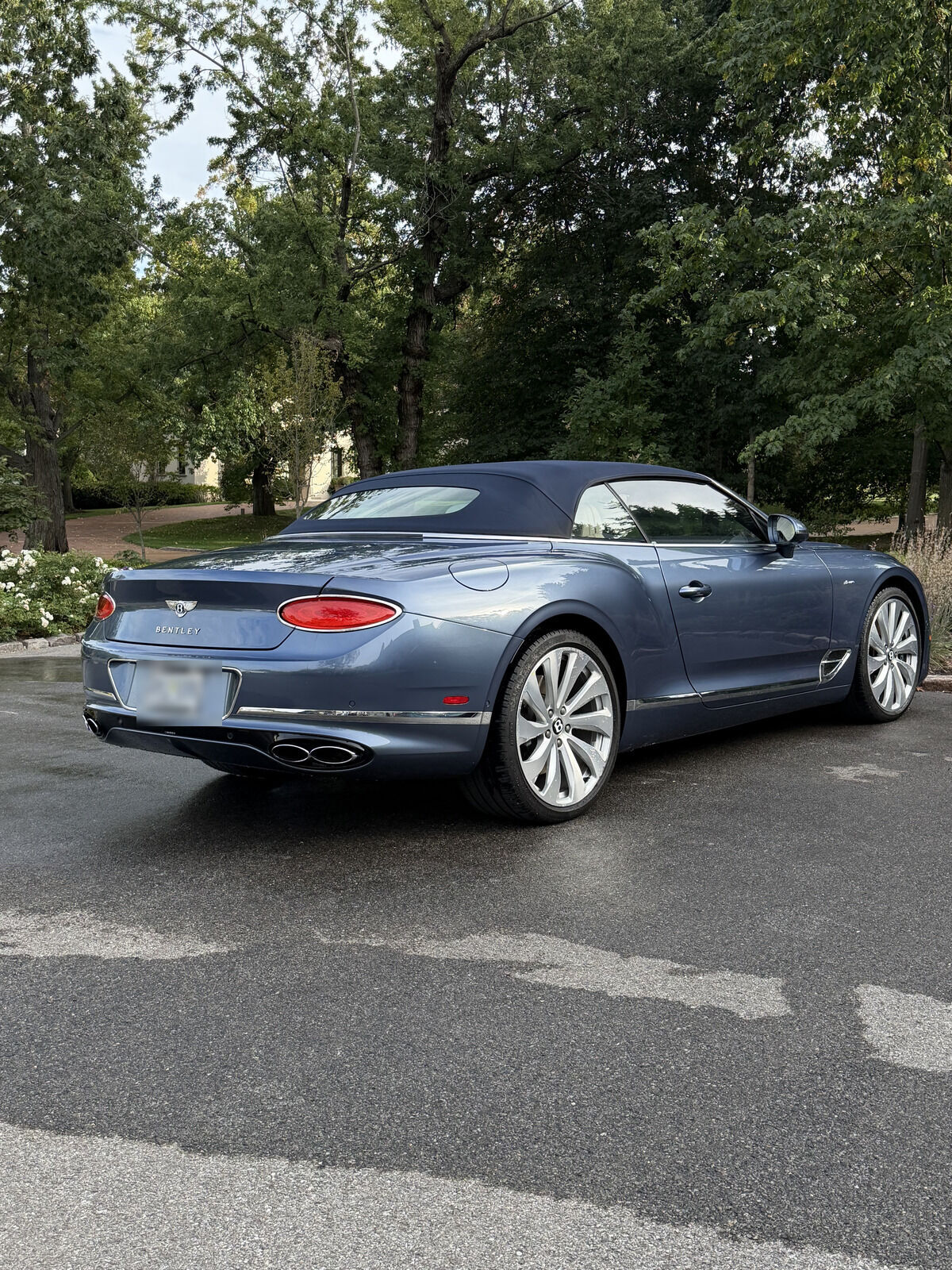 Blue Bentley Continental GT convertible with its roof up, freshly detailed on wet pavement
