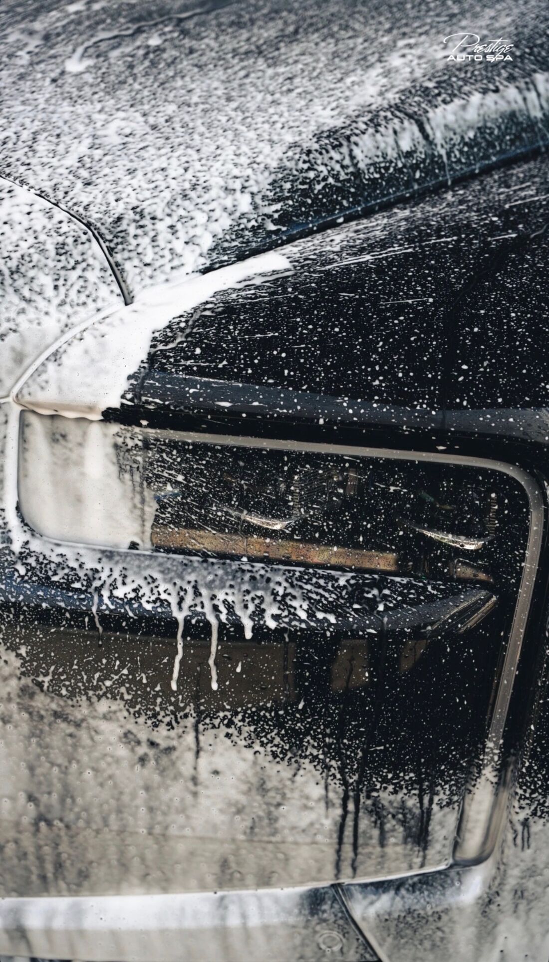 Thick white foam dripping across a black SUV's headlight and hood