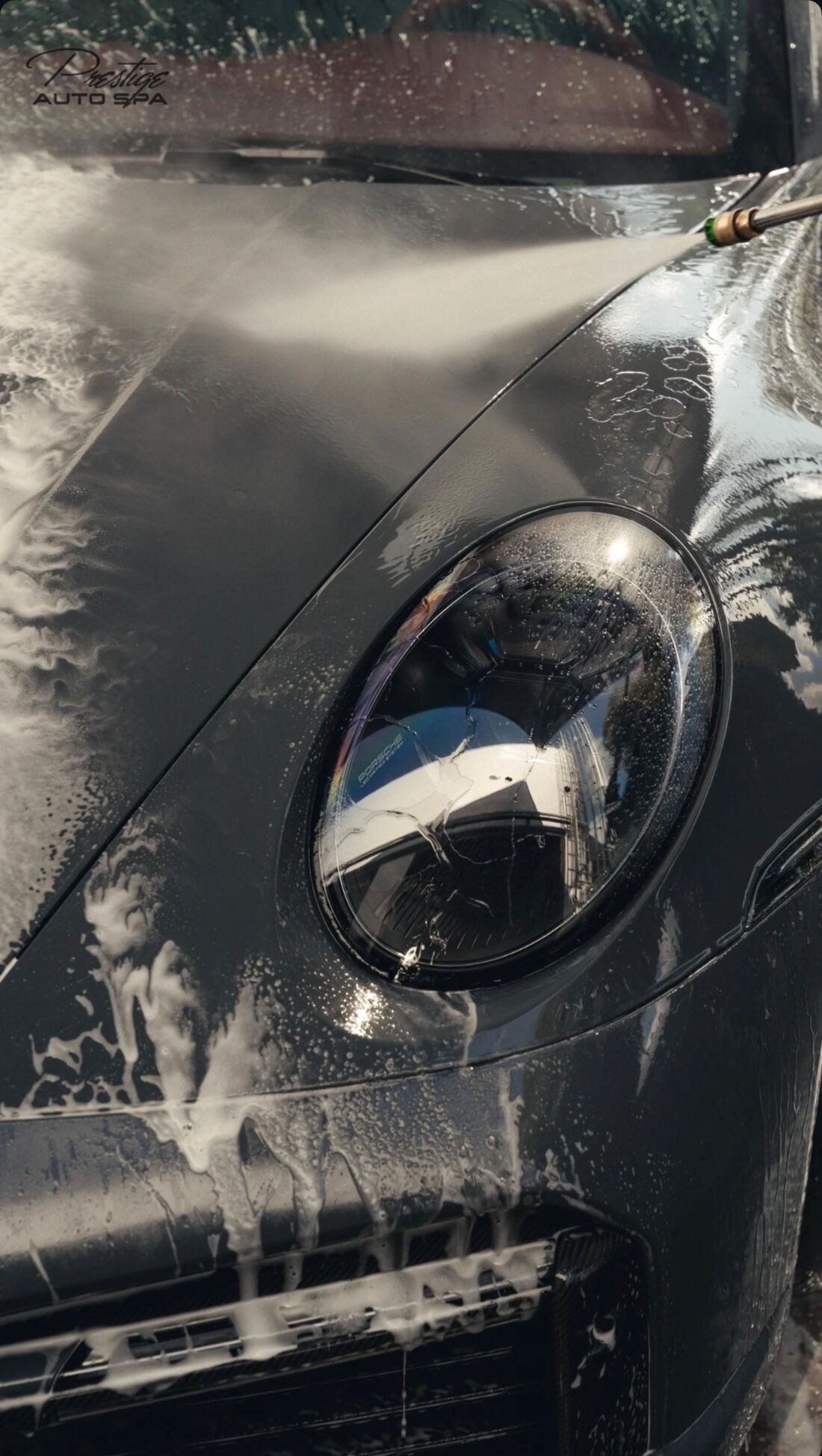 Soap rinsing off a dark Porsche 911 headlight under a pressure washer